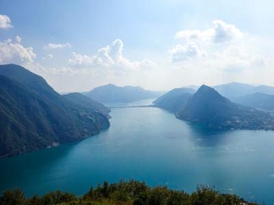 Breathtaking aerial view of Lake Lugano surrounded by lush mountains and clear blue skies.