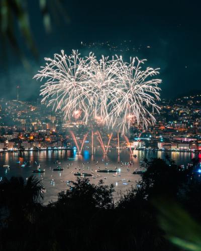 Vibrant fireworks display lighting up the night sky over Lugano, Switzerland, reflecting beautifully over the lake.