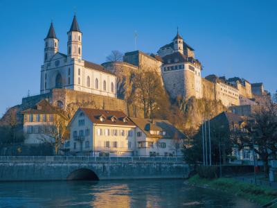 Aarburg Castle, a historic landmark, towers over a serene river and picturesque Swiss town in soft evening light.