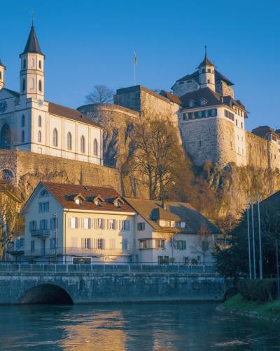 Aarburg Castle, a historic landmark, towers over a serene river and picturesque Swiss town in soft evening light.