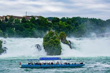 Tourists enjoy a scenic boat ride below Switzerland's stunning Rhine Falls.