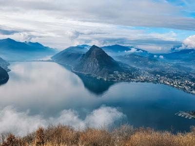 Aerial view of Lake Lugano surrounded by mountains and clouds, offering breathtaking scenery.