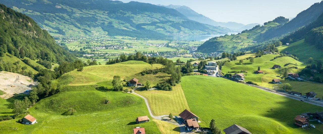 A breathtaking aerial view of the lush Swiss countryside, featuring hills and houses under a clear blue sky.