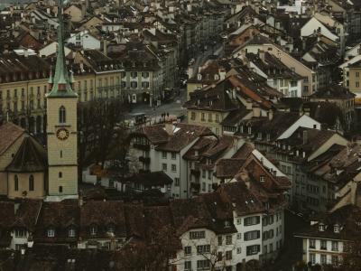 A view of the Aare River in Bern, Switzerland, featuring the historic Nydeggbrücke bridge and traditional buildings with terracotta roofs along the riverbank.
