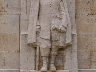 A stone relief sculpture of a man in 17th-century attire holding a book, with the name "ROGER WILLIAMS" inscribed on the base, set within a larger stone wall featuring other inscriptions.