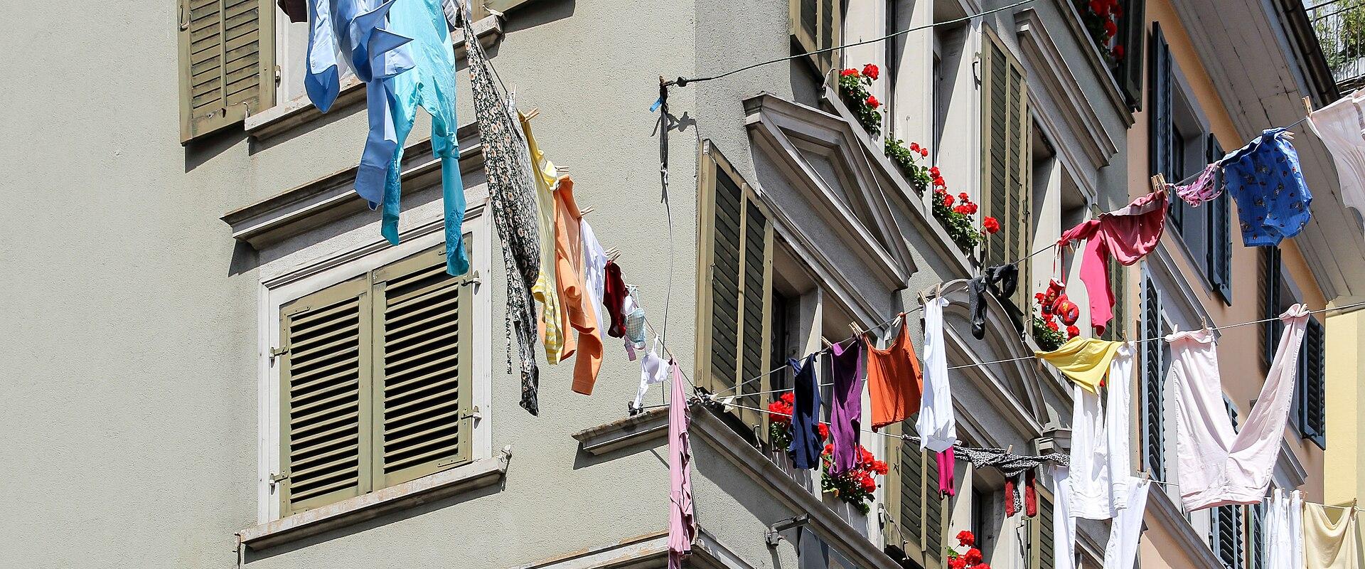 A close-up view of laundry hanging on lines strung between the facades of multi-story buildings with shuttered windows and flower boxes.