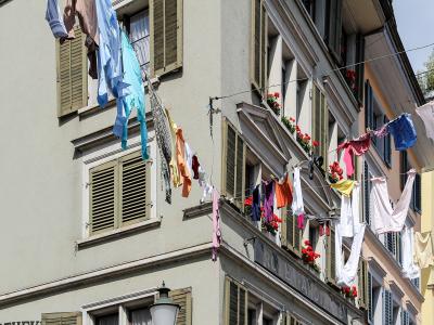 A close-up view of laundry hanging on lines strung between the facades of multi-story buildings with shuttered windows and flower boxes.