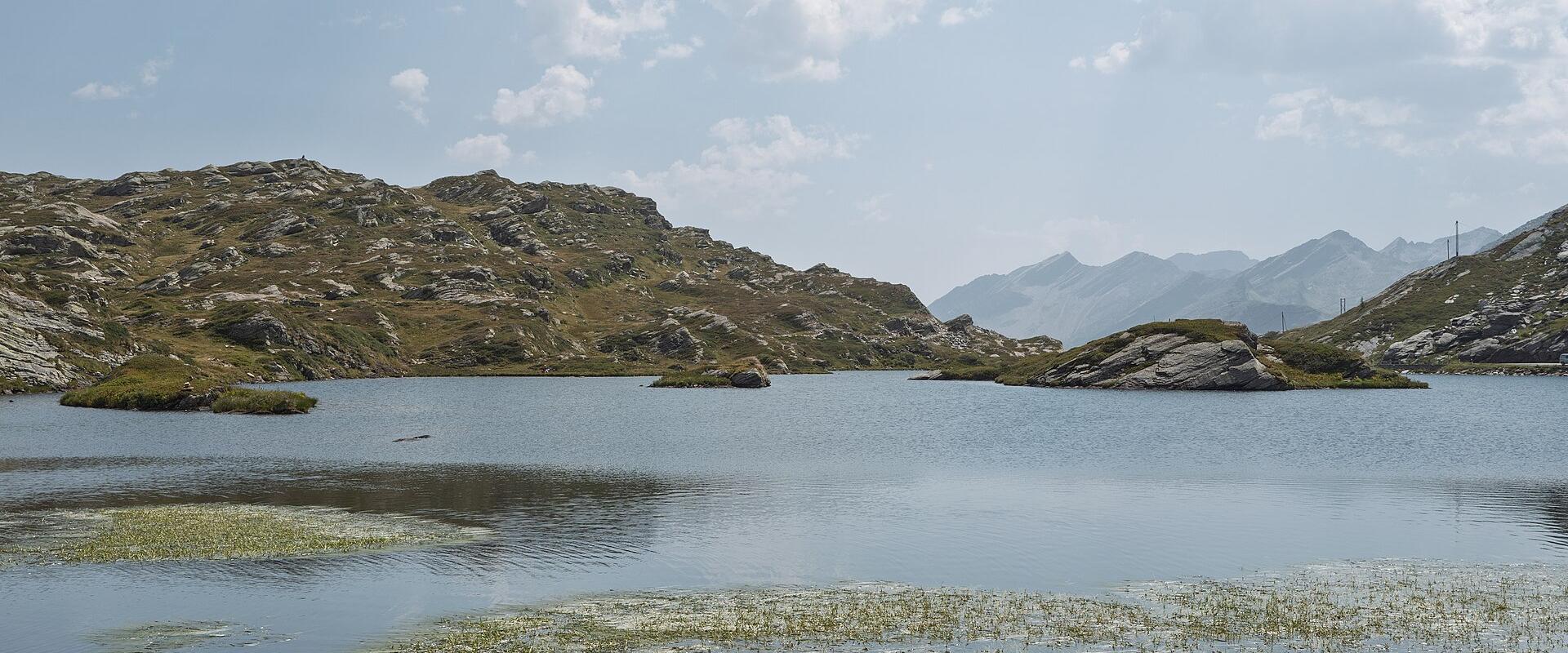 A high-altitude alpine lake with rocky shores and grassy banks, featuring two overturned rowboats in the foreground, one marked with "2066 M." and "SAN BERNARDINO".
