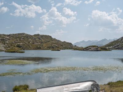 A high-altitude alpine lake with rocky shores and grassy banks, featuring two overturned rowboats in the foreground, one marked with "2066 M." and "SAN BERNARDINO".