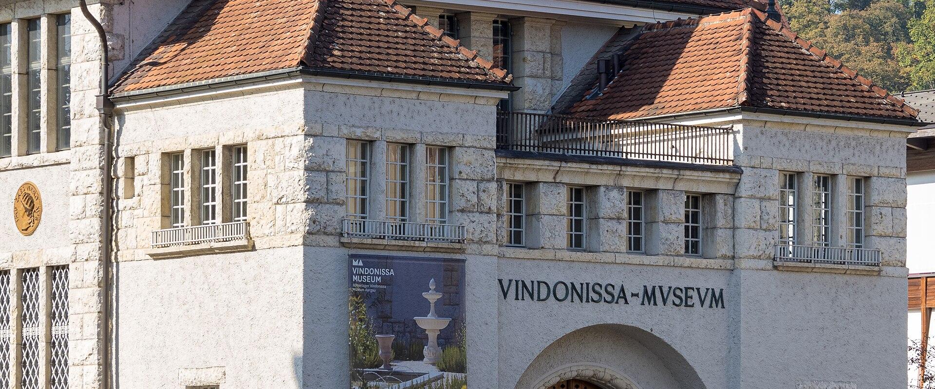 A white stone building with a red tiled roof, featuring the large inscription "VINDONISSA-MVSEVM" above an arched entrance and a vertical sign on the right reading "VINDONISSA MUSEUM".