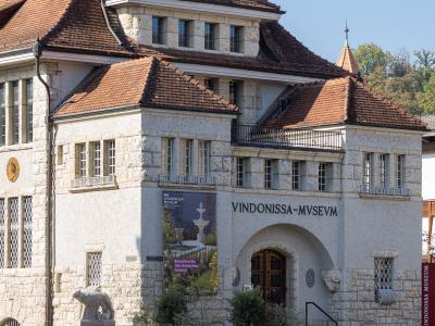 A white stone building with a red tiled roof, featuring the large inscription "VINDONISSA-MVSEVM" above an arched entrance and a vertical sign on the right reading "VINDONISSA MUSEUM".