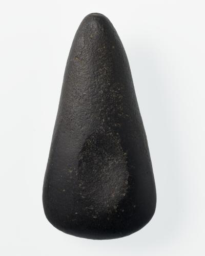 A studio photograph of a dark, polished stone axe head (stone adze) against a plain white background.