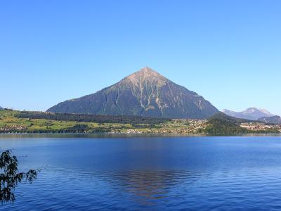 A wide landscape shot showing a large, pyramid-shaped mountain rising above a lake and a town on the shore under a clear blue sky.