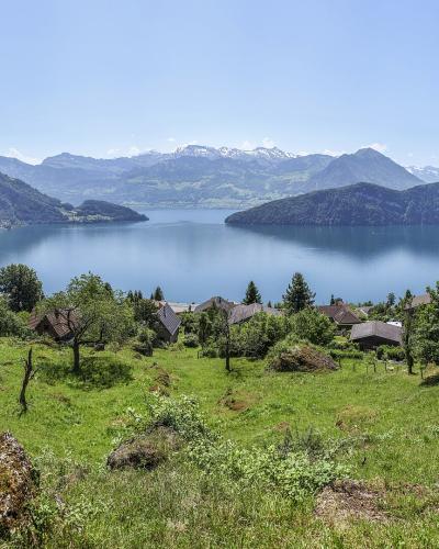 A scenic landscape view of a large lake surrounded by green hills and mountains, with a red house visible on the right slope.