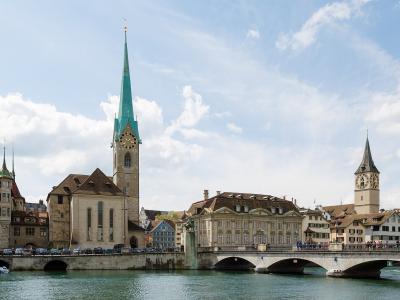 A view of the Limmat River in Zürich's Old Town featuring the Fraumünster church with its distinctive green spire on the left and the Münsterbrücke bridge in the foreground.