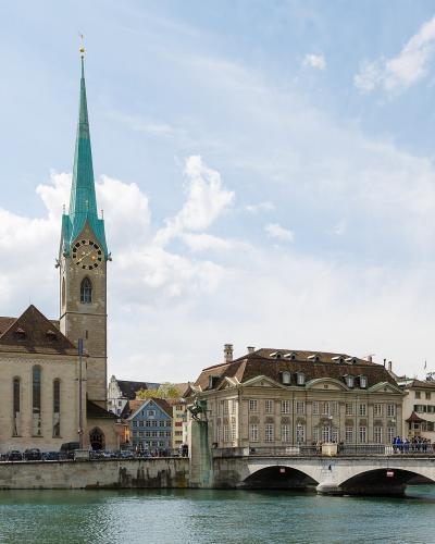 A view of the Limmat River in Zürich's Old Town featuring the Fraumünster church with its distinctive green spire on the left and the Münsterbrücke bridge in the foreground.
