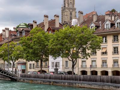 A panoramic view of the city of Bern, Switzerland, showing the Aare River winding through the old town with the Zytglogge tower and the Münster cathedral visible, taken from an elevated position.