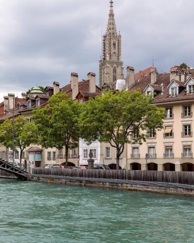 A panoramic view of the city of Bern, Switzerland, showing the Aare River winding through the old town with the Zytglogge tower and the Münster cathedral visible, taken from an elevated position.