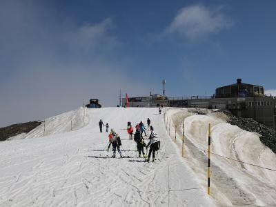 A group of skiers on a snowy slope leading up to a mountain station building with a rotating restaurant structure on the right.