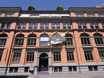 A peach-colored historic building facade with a large white lace installation hanging from the second-story windows and a sign for "café bar st.gall" near the entrance.