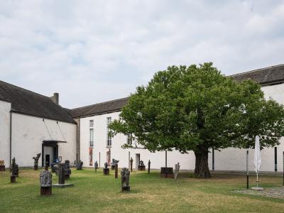 A courtyard with white buildings, a large tree, and various sculptures on display.