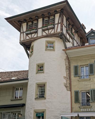 A low-angle shot of a distinctive white cylindrical tower with a projecting upper story featuring timber framing and flower boxes, situated between other buildings in an urban setting.