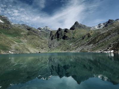 A high-altitude alpine lake surrounded by steep, rocky mountain slopes with patches of snow and green vegetation, reflecting the peaks in the calm water.
