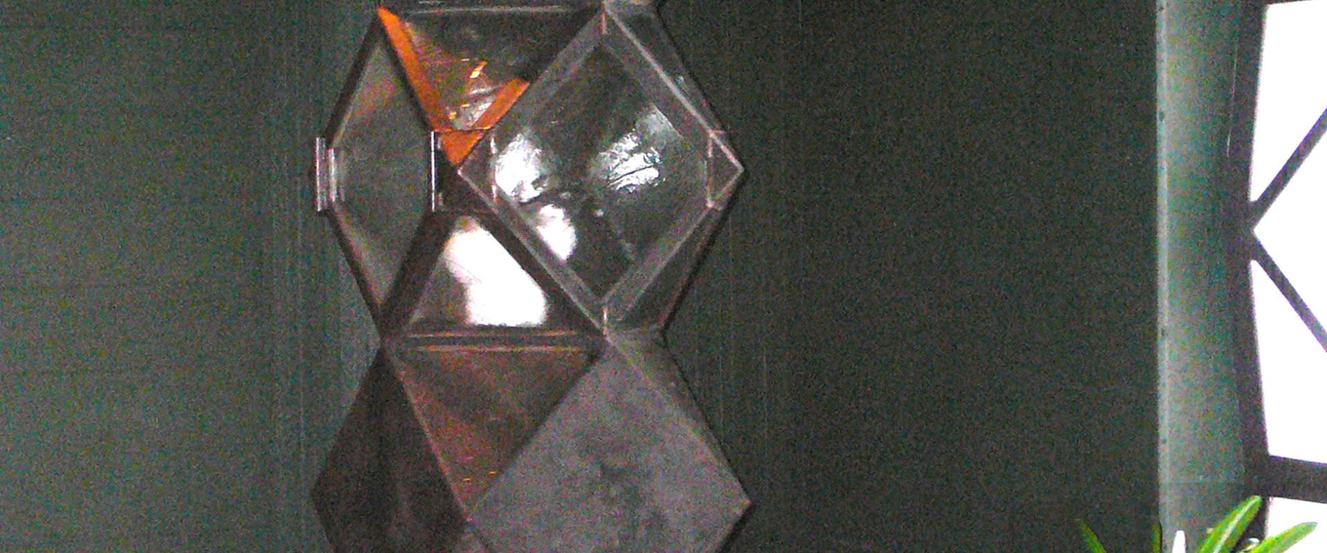 A close-up interior shot of a modern, geometric tabernacle made of stacked, reflective metallic cubes, situated next to potted white orchids and a window with a dark frame.