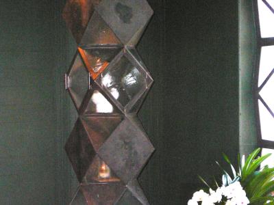 A close-up interior shot of a modern, geometric tabernacle made of stacked, reflective metallic cubes, situated next to potted white orchids and a window with a dark frame.