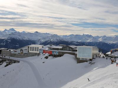 A high-altitude ski resort complex featuring modern buildings, a snow park area with ramps, and skiers on slopes, set against a backdrop of the Pennine Alps.