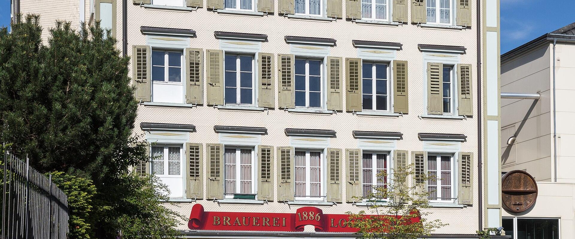 A multi-story cream-colored building with green shutters and a prominent red sign reading "BRAUEREI 1886 LOCHER" on the facade.