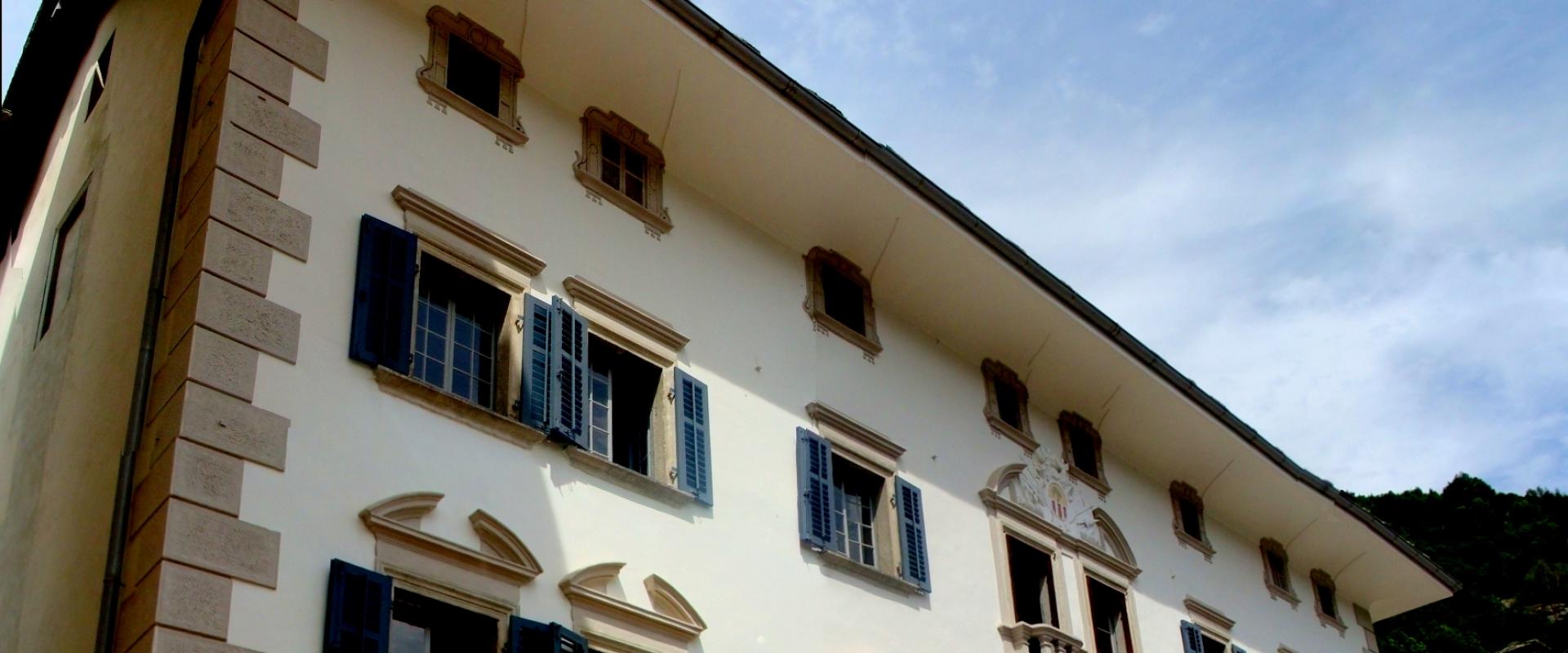 A low-angle shot of a large, white-walled historic building with blue shutters, stone quoins, and signage reading "ALBERGO" and "RISTORANTE" above the ground floor windows.