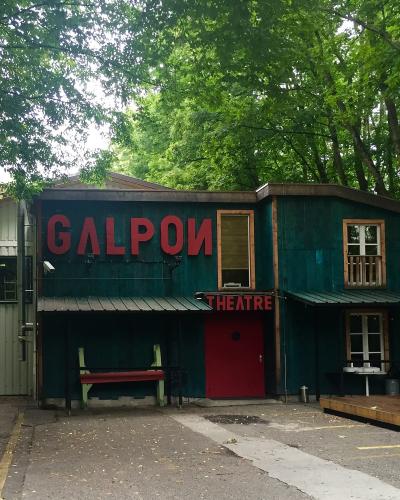 A teal wooden building with large red letters spelling "GALPON" and smaller red letters spelling "THEATRE" on the facade, surrounded by trees.