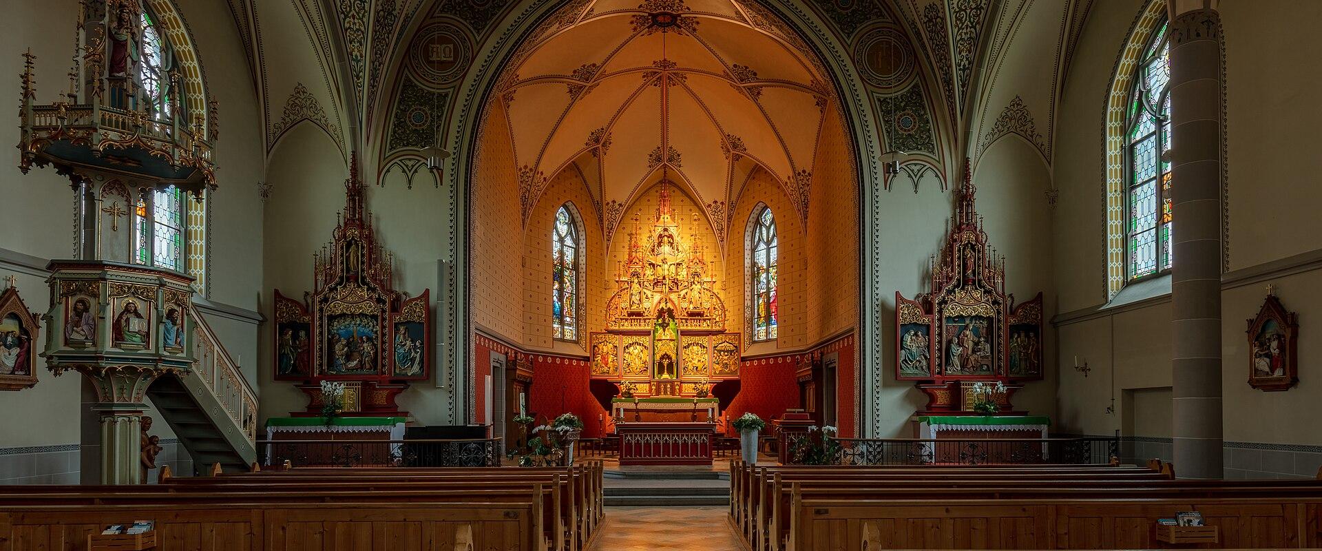 The interior of a Catholic church featuring a central nave with wooden pews, an ornate gilded high altar, side altars, a pulpit on the left, and vaulted ceilings with decorative frescoes.