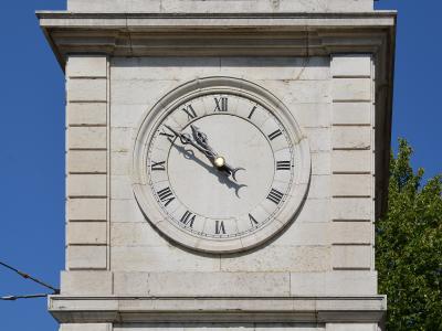 A close-up view of a stone clock tower face with Roman numerals, ornate hands, and a sun/moon indicator against a blue sky.
