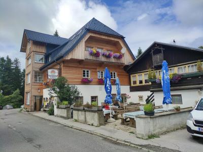 A traditional wooden Alpine inn with flower boxes on the balcony, outdoor seating with blue umbrellas, and a hanging sign reading "Alpenhotel Passhöhe".