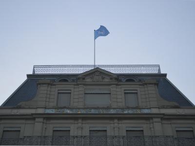 The image shows the upper facade of a classical stone building with a mansard roof, a United Nations flag flying on a pole, and the inscription "PALAIS WILSON" in gold lettering above the windows.