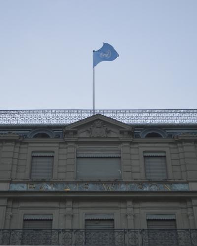 The image shows the upper facade of a classical stone building with a mansard roof, a United Nations flag flying on a pole, and the inscription "PALAIS WILSON" in gold lettering above the windows.