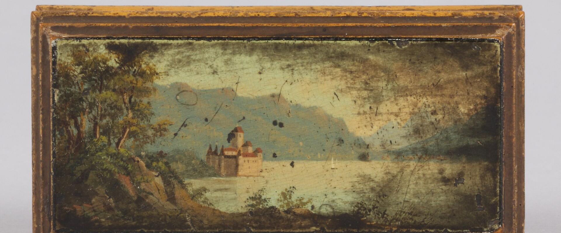 A rectangular antique wooden box with a painted miniature landscape on its lid depicting a castle on a lake shore with mountains in the background.