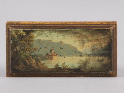A rectangular antique wooden box with a painted miniature landscape on its lid depicting a castle on a lake shore with mountains in the background.