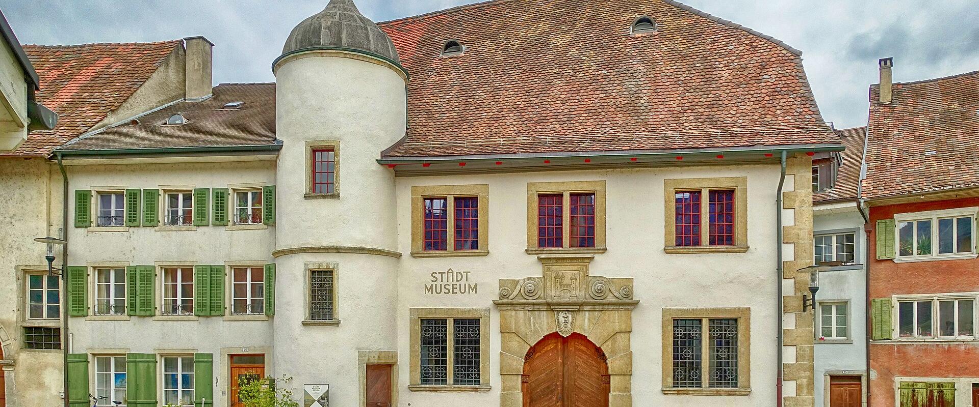 A historic white building with a round tower and a large wooden gate, featuring the text "STADT MUSEUM" on the facade.