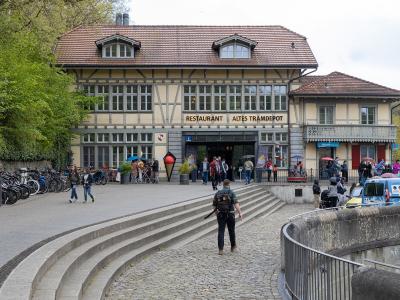 A large, two-story building with a traditional Swiss architectural style, featuring a prominent sign above the entrance that reads "RESTAURANT ALTES TRAMDEPOT", with people and bicycles in the foreground.