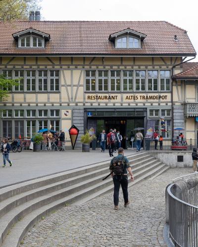 A large, two-story building with a traditional Swiss architectural style, featuring a prominent sign above the entrance that reads "RESTAURANT ALTES TRAMDEPOT", with people and bicycles in the foreground.