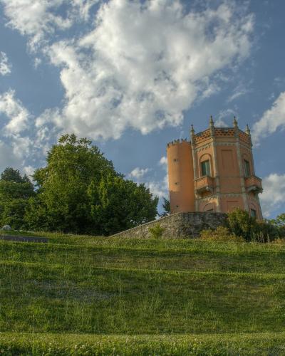 A low-angle shot of a grassy hillside leading up to a distinctive pinkish-orange, castle-like tower with crenellations and turrets, set against a blue sky with white clouds.