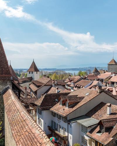 A view from a stone wall overlooking the red-tiled roofs and defensive towers of a historic European town, with a large lake visible in the background.