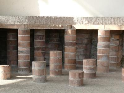 The image shows a series of cylindrical brick pillars (pilae) supporting a stone slab floor, which is the characteristic structure of a Roman hypocaust underfloor heating system.