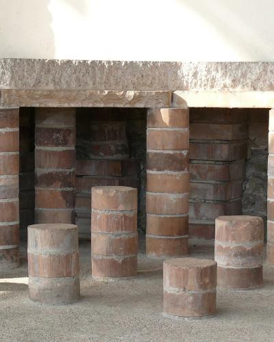 The image shows a series of cylindrical brick pillars (pilae) supporting a stone slab floor, which is the characteristic structure of a Roman hypocaust underfloor heating system.