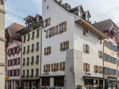 A street-level view of a white corner building with distinctive yellow and black striped shutters and the word "LATERNE" on the facade, located on a cobblestone street with other historic buildings.